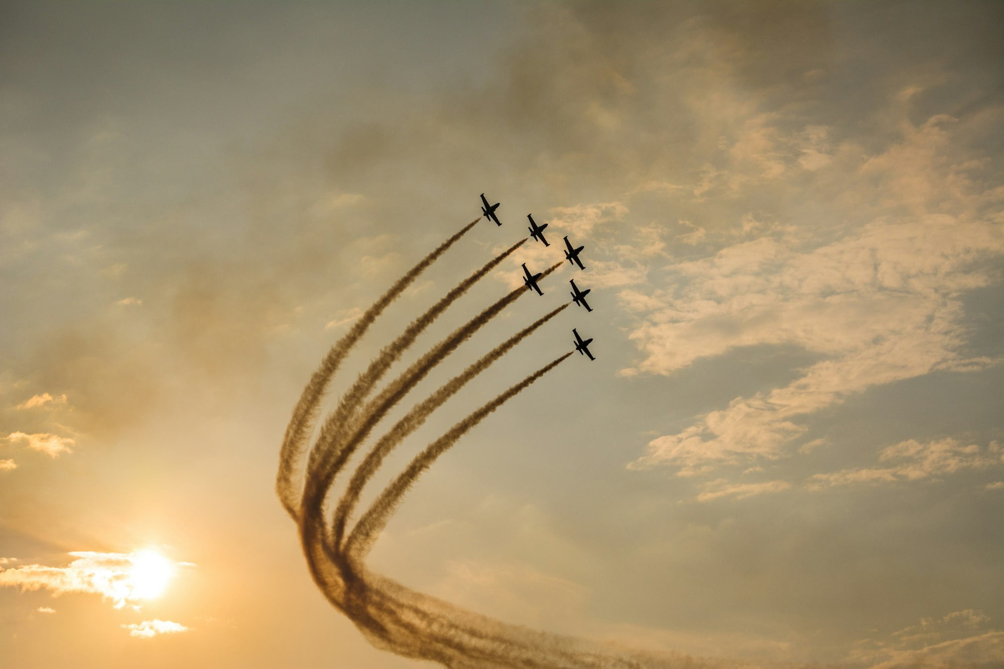 Six aircraft flying in formation with smoke trails at sunset.